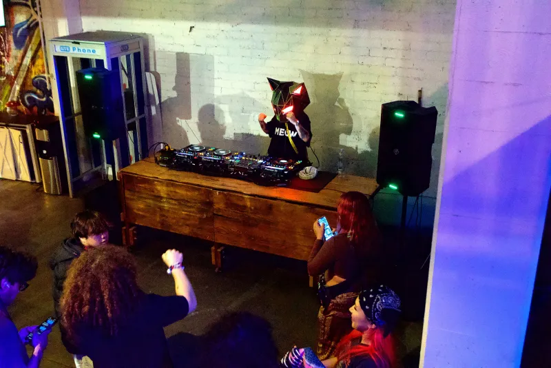 A DJ at the booth under the screen and colored light in the Back Venue at 1712 Studios