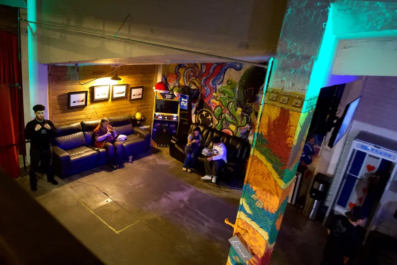 The Back Venue lounge at 1712 Studios lit purple and green at night, couches and the mural