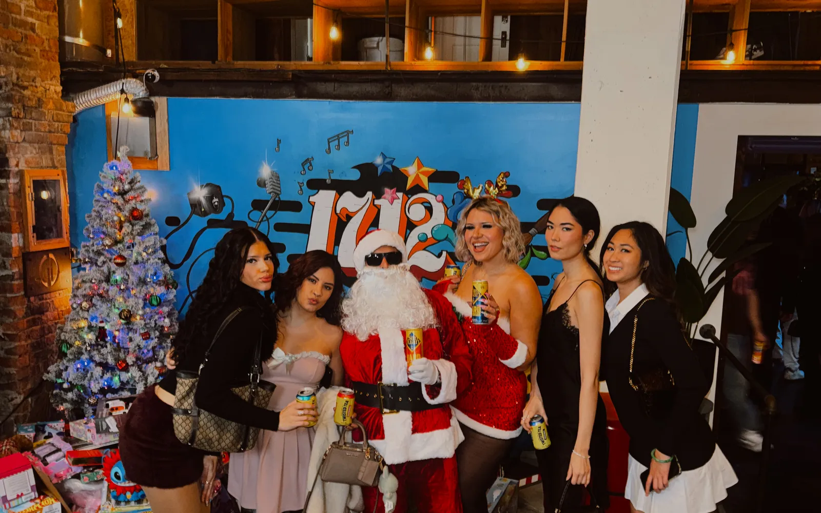 Santa with five guests in front of the 1712 mural and the lit holiday tree in the Back Venue at 1712 Studios