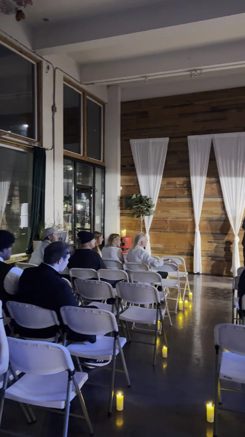 Guests seated for a candlelit evening ceremony by the wood wall in the Main Hall at 1712 Studios