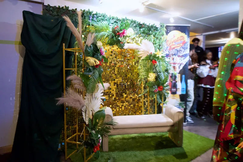 A flower wall photo spot with a bench and gold sequin backdrop in the Main Hall at 1712 Studios