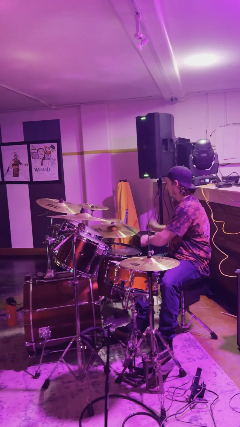 A drummer and band playing under purple light in the Main Hall at 1712 Studios