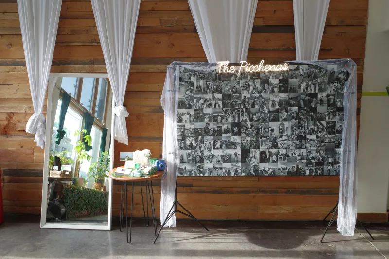 A wedding photo backdrop with a neon name sign and white drapes against the wood wall in the Main Hall at 1712 Studios, photo by Megan Roling